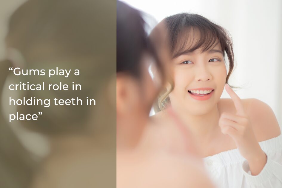A woman smiles in a mirror while pointing to her teeth; text on the left reads, “Healthy gums play a critical role in holding teeth in place and supporting oral wellness.”.