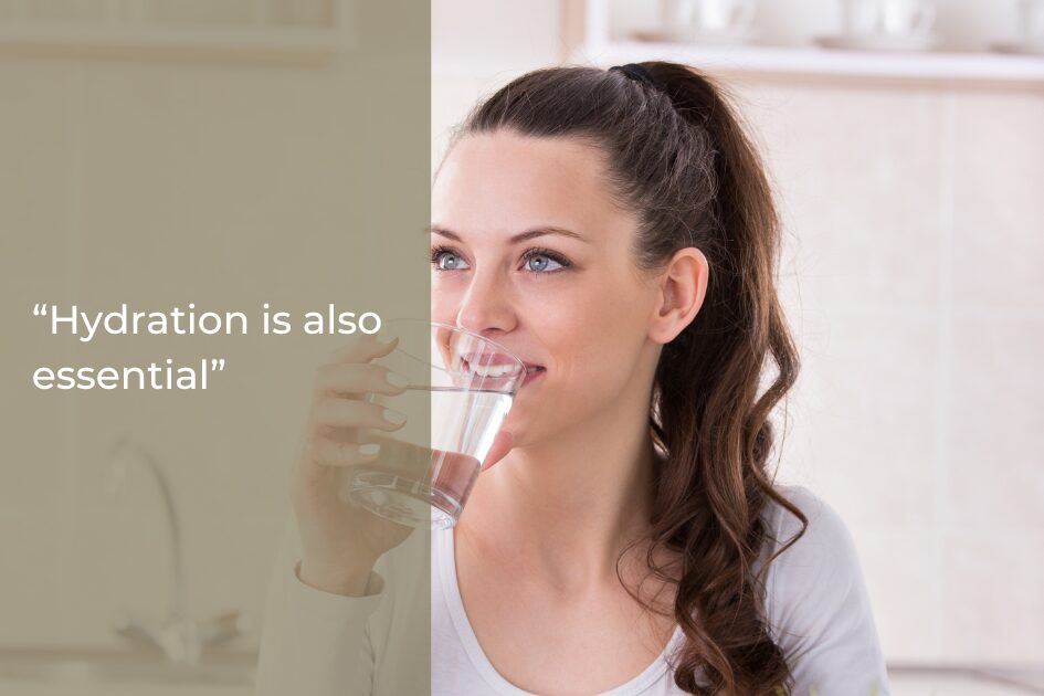 A woman with a ponytail drinks a glass of water in a kitchen; text overlay reads "Hydration is also essential for gum health.